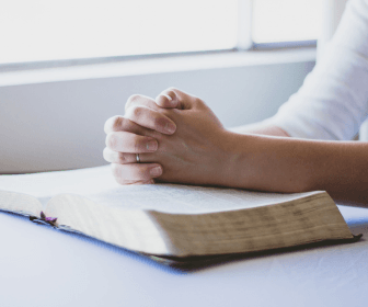 hands folded in prayer over a bible
