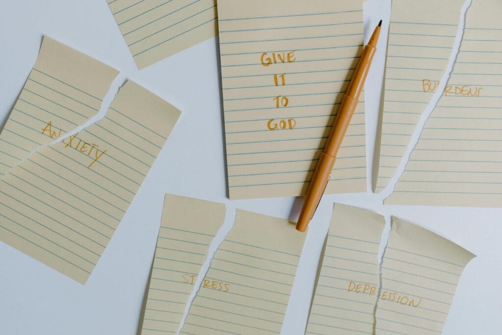 lay down your burdens Ripped notebook pages with words anxiety, stress, depression, give it to God and a pen on a table.