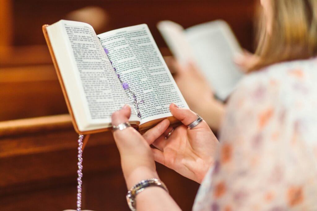 pexels-photo-8674183-8674183 A woman holding a Bible and rosary beads, engaged in prayer inside a church.