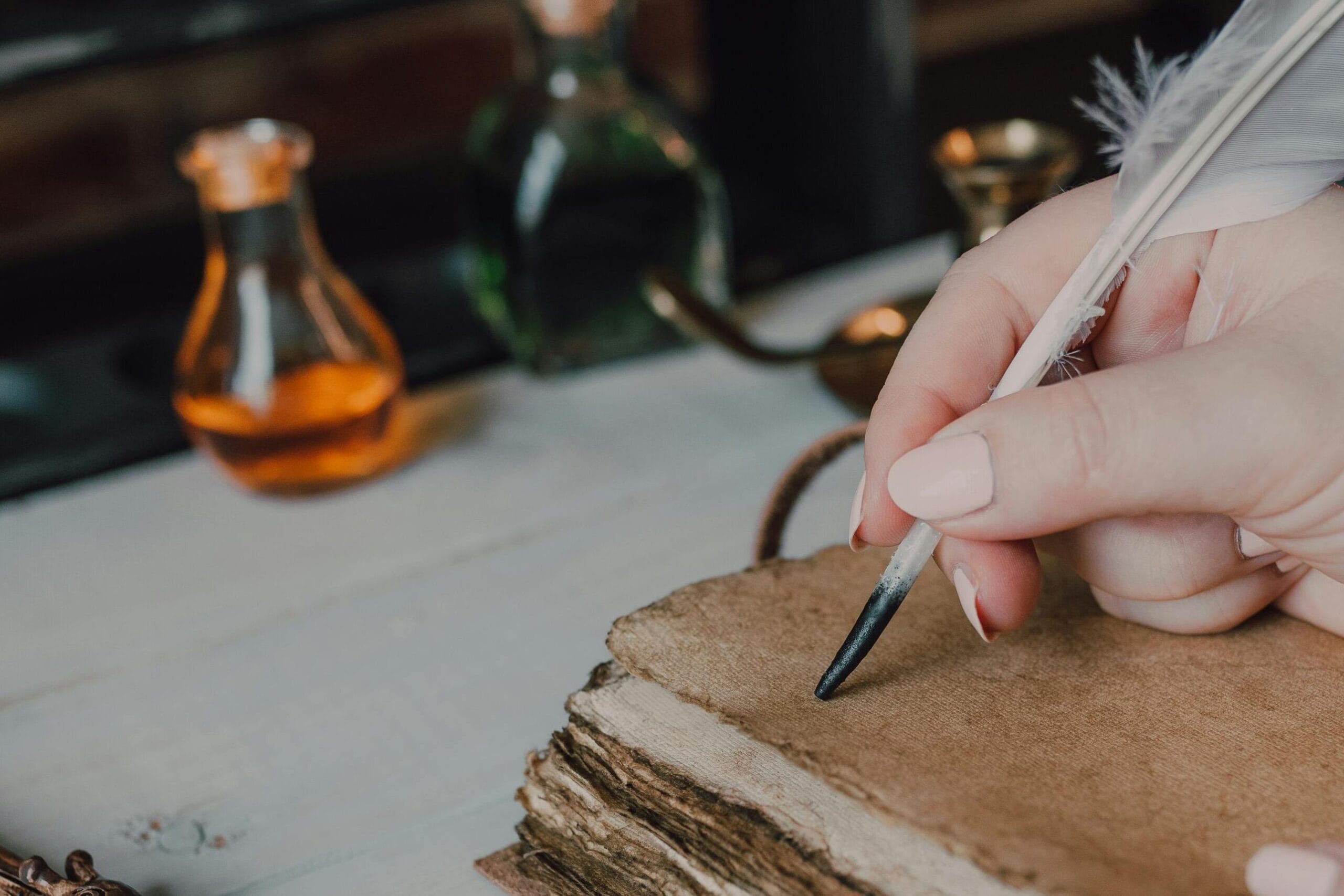 Close-up of hands writing with a quill in a spellbook, featuring magical items and a wand.