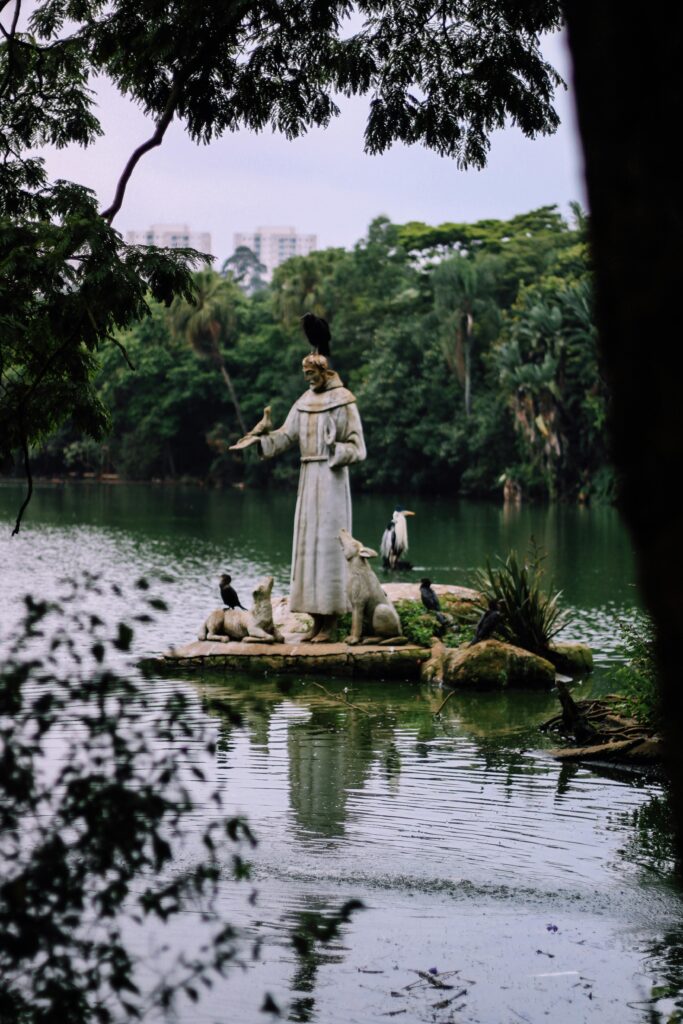 Statue of Saint Francis surrounded by birds and lush greenery on a lake island.