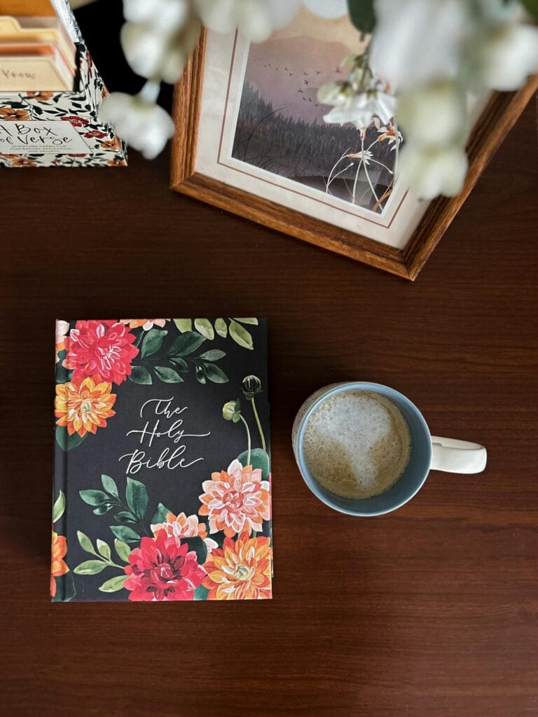 Top view of a floral bible and coffee cup on a wooden table, inviting relaxation and reflection.